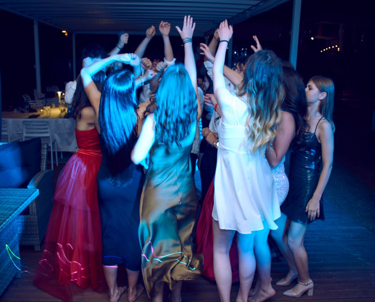 Group of young women dancing together with hands raised at an outdoor evening party.