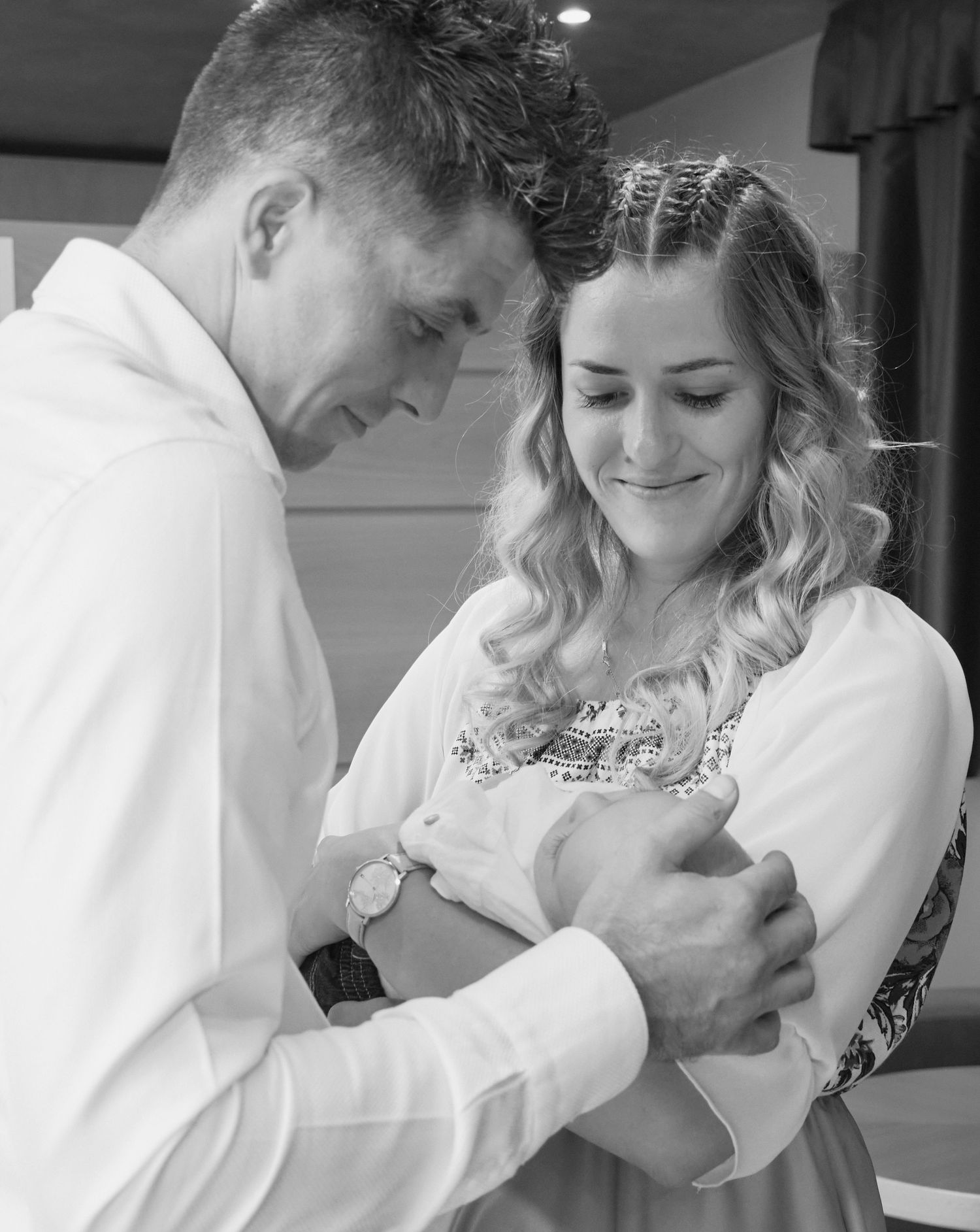 Black and white photo of young couple gazing lovingly at their newborn baby during christening celebration.