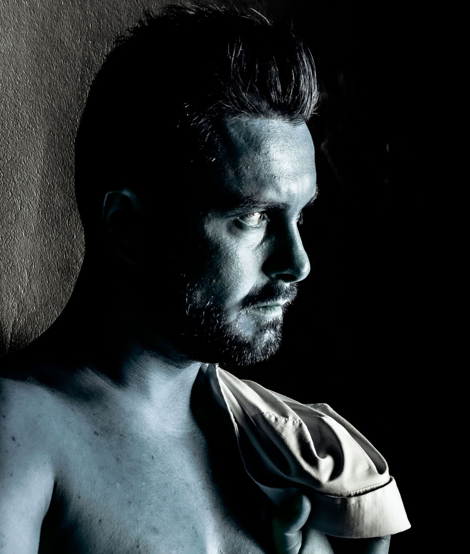 Dramatic black and white portrait of a bearded shirtless man in shadow.