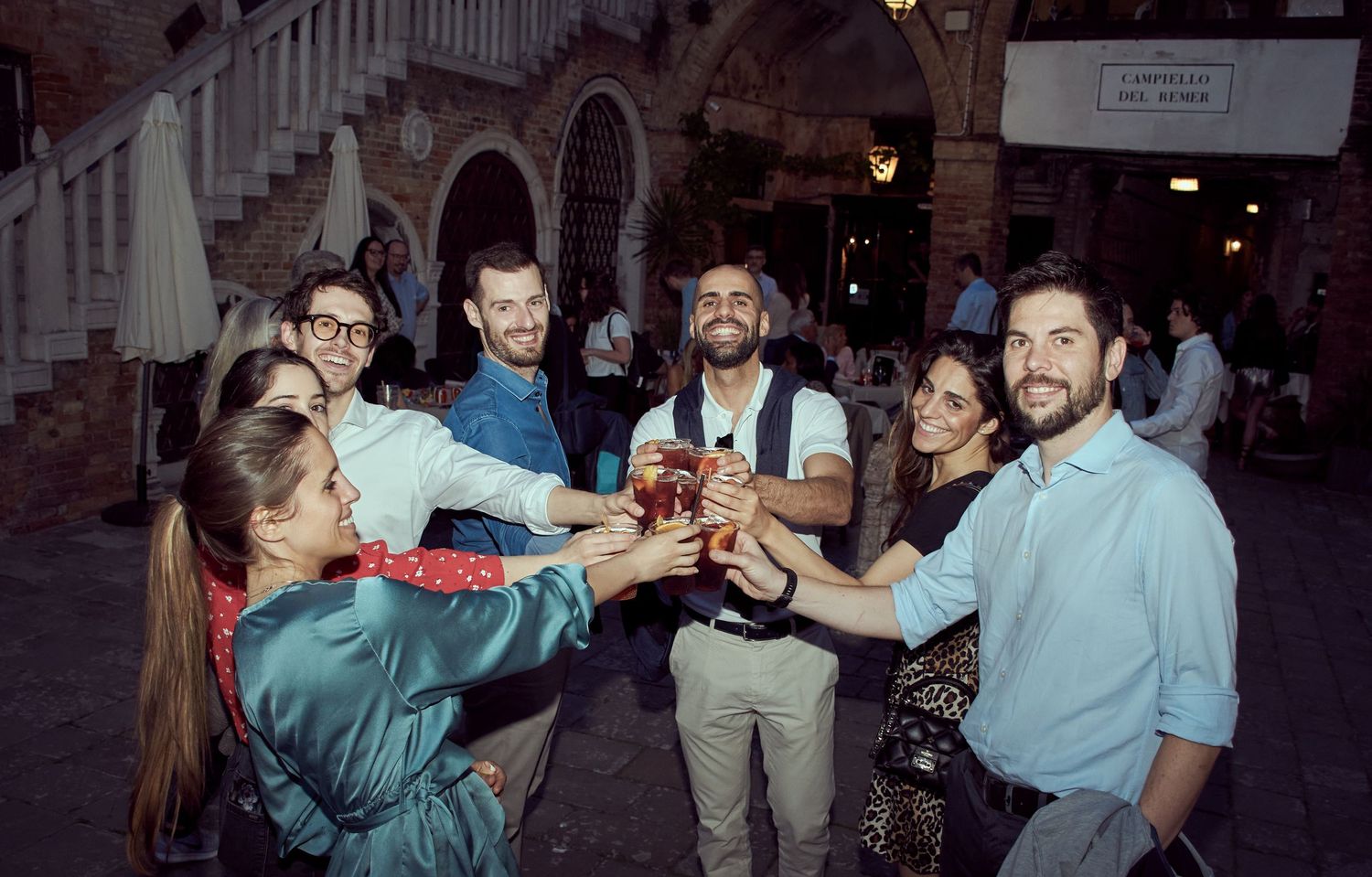 Group of friends toasting drinks outdoors at night in a historic Italian piazza.