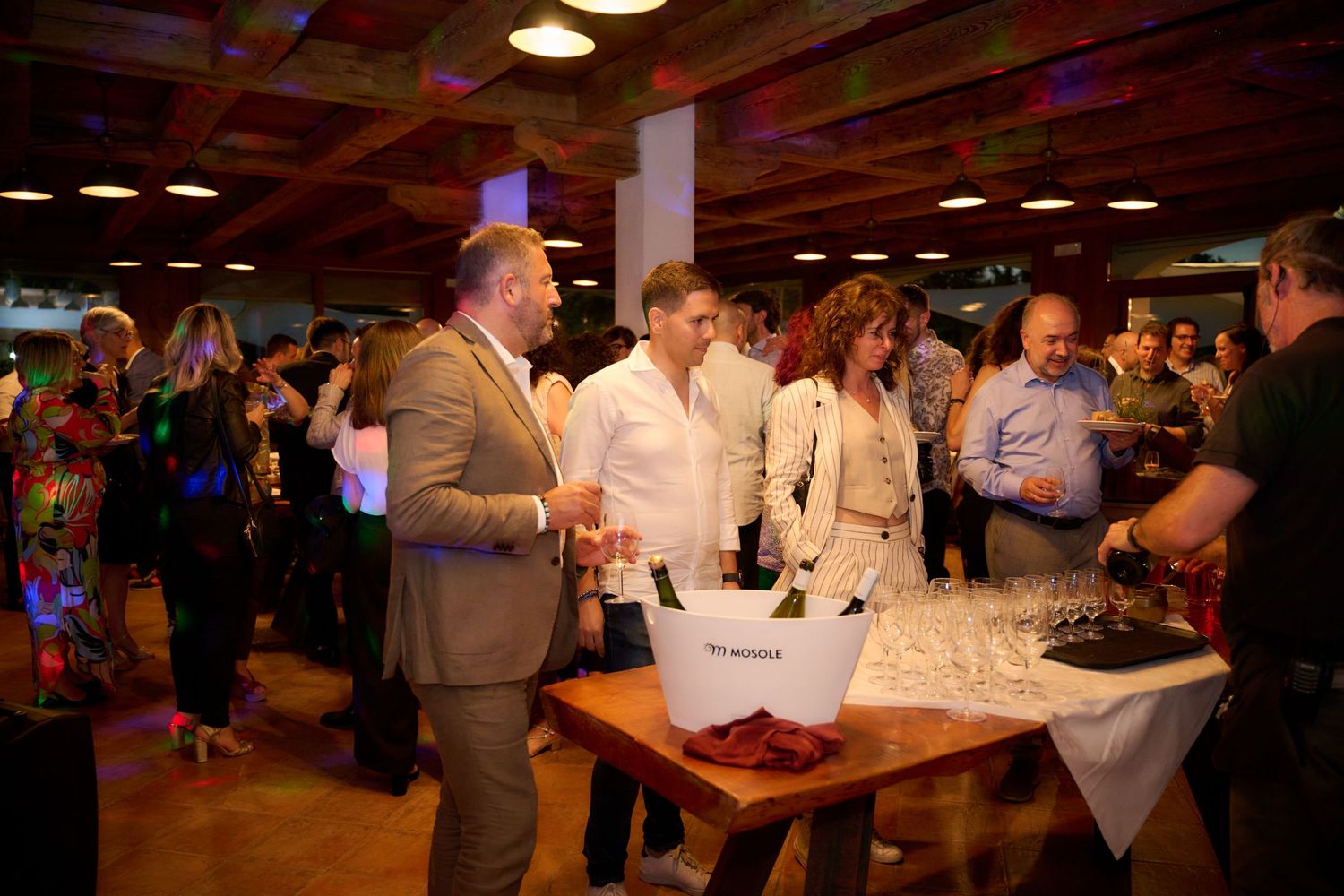 Guests mingle at an elegant indoor party with champagne on ice at a wooden table.