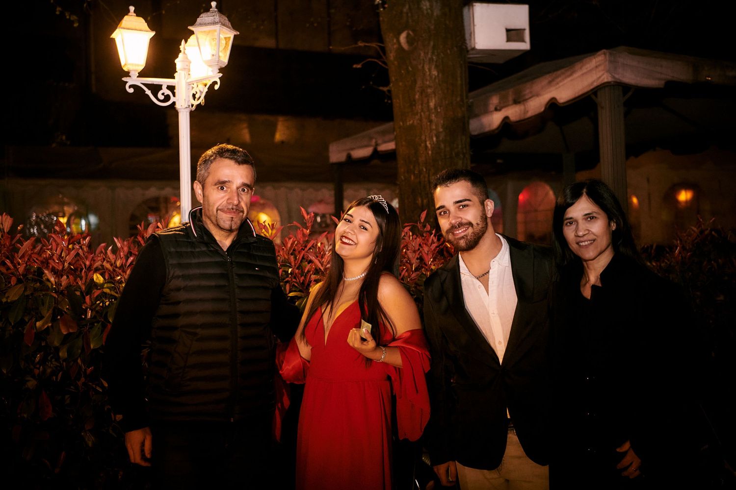 Two couples posing together outdoors at night near decorative garden lighting.