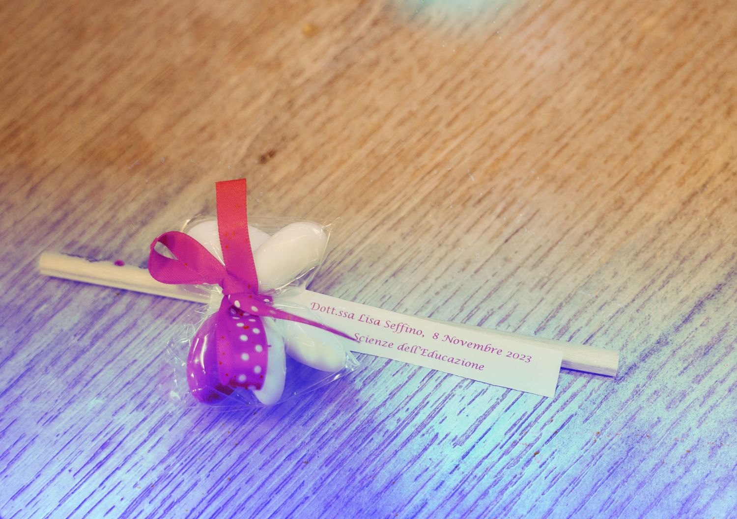Personalized fortune cookie wedding favor with pink ribbon bow on wooden table with purple lighting.
