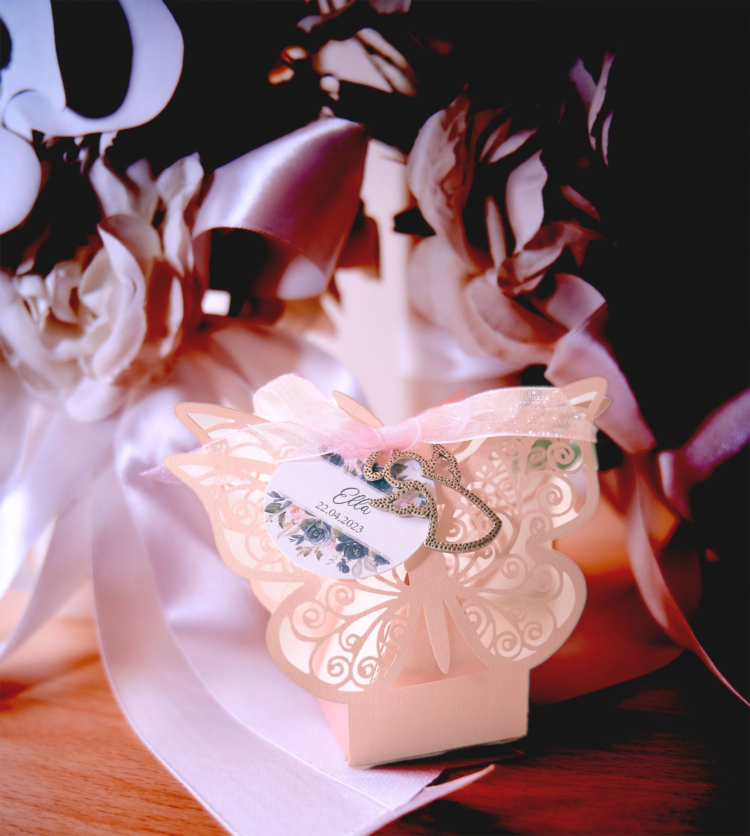 Elegant butterfly-shaped pink laser-cut wedding favor box with ribbon and floral tag on wooden surface.