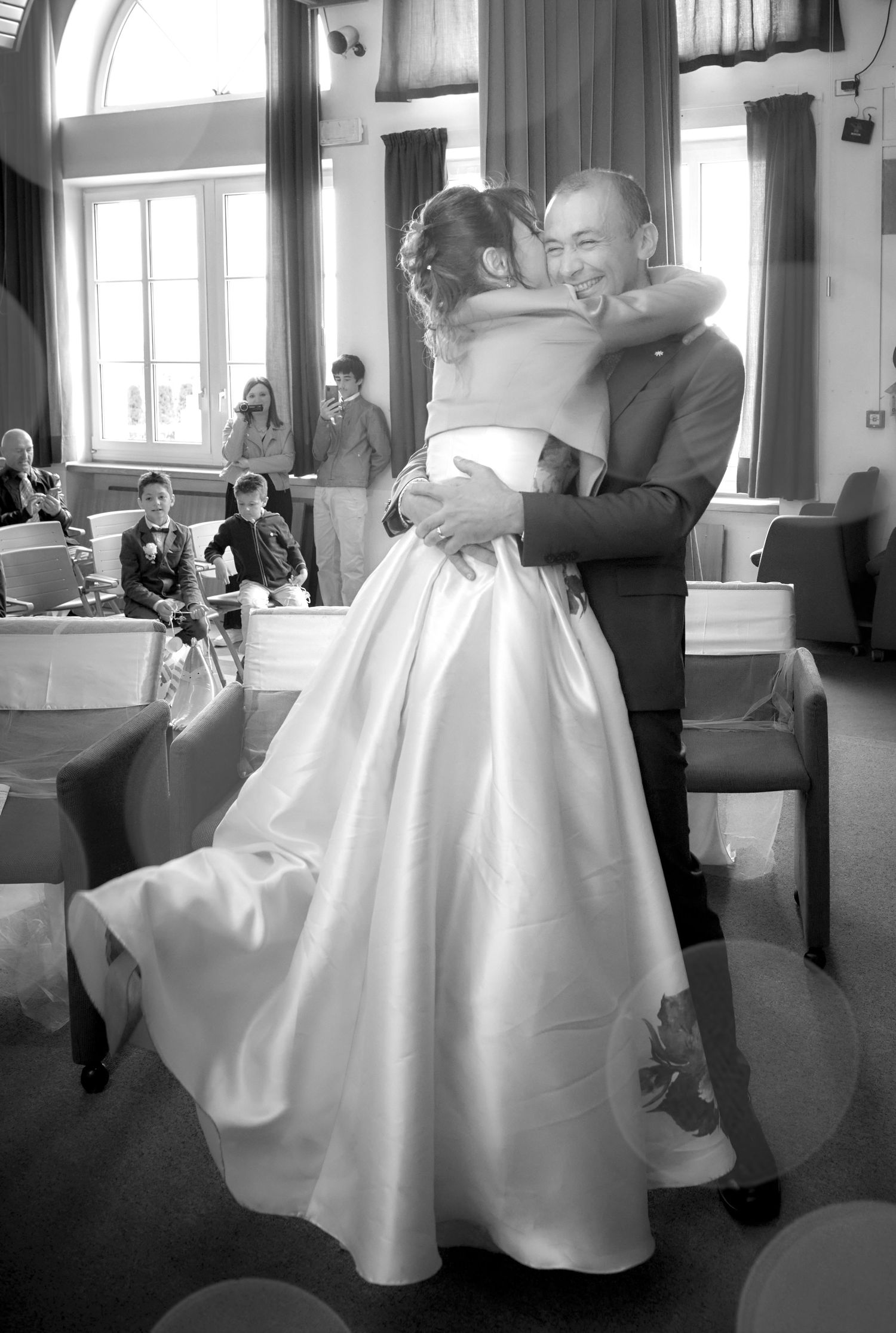 Groom joyfully lifts bride in a stunning white satin gown during their wedding celebration.