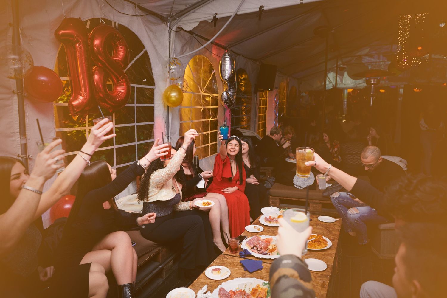 Group of friends toasting and celebrating at a festive indoor party with red balloons.