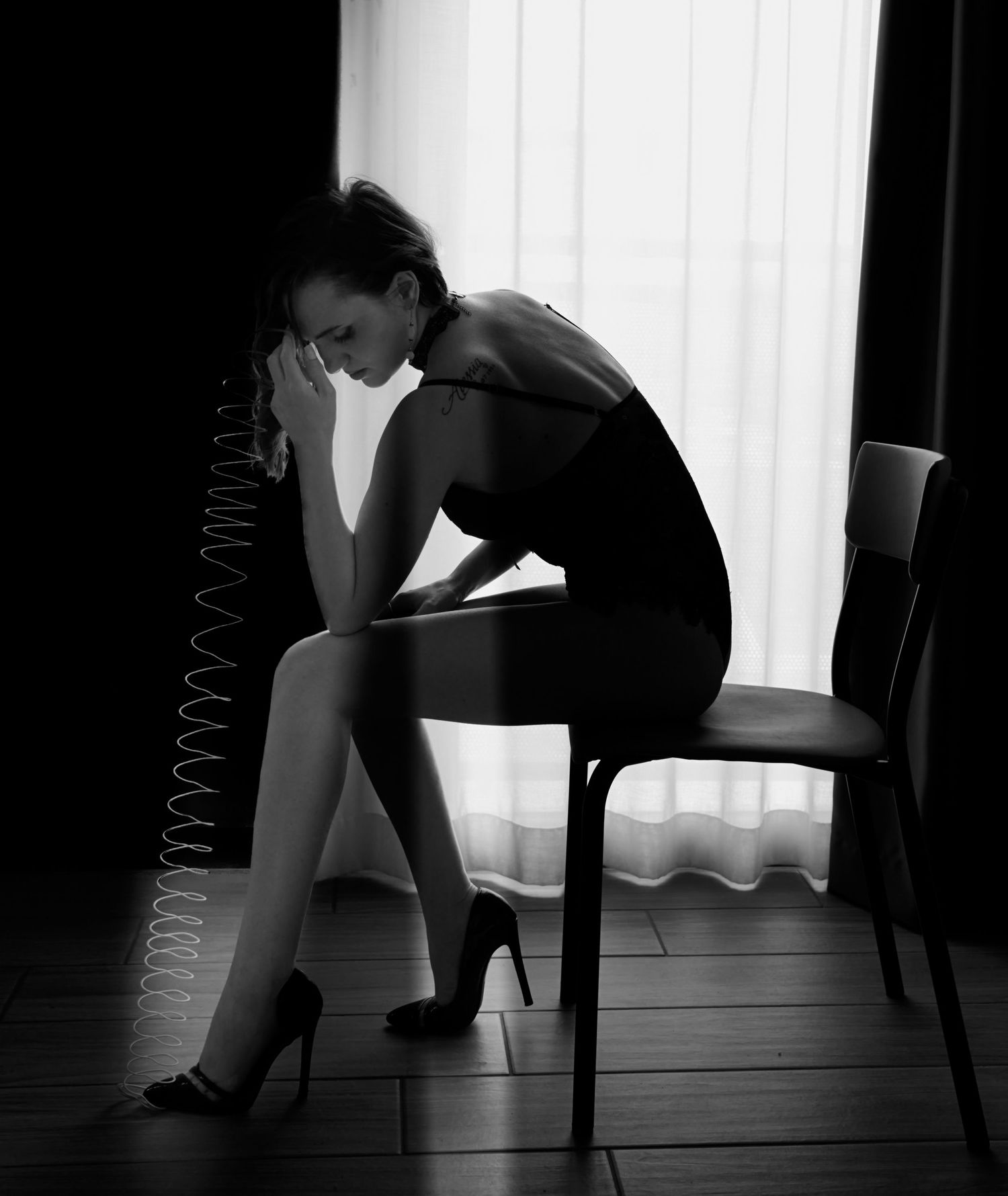 Black and white artistic photo of woman in black dress sitting at table holding vintage phone.