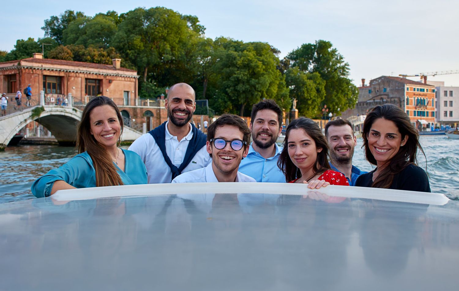 Group of seven friends posing together on a boat on a Venice canal.