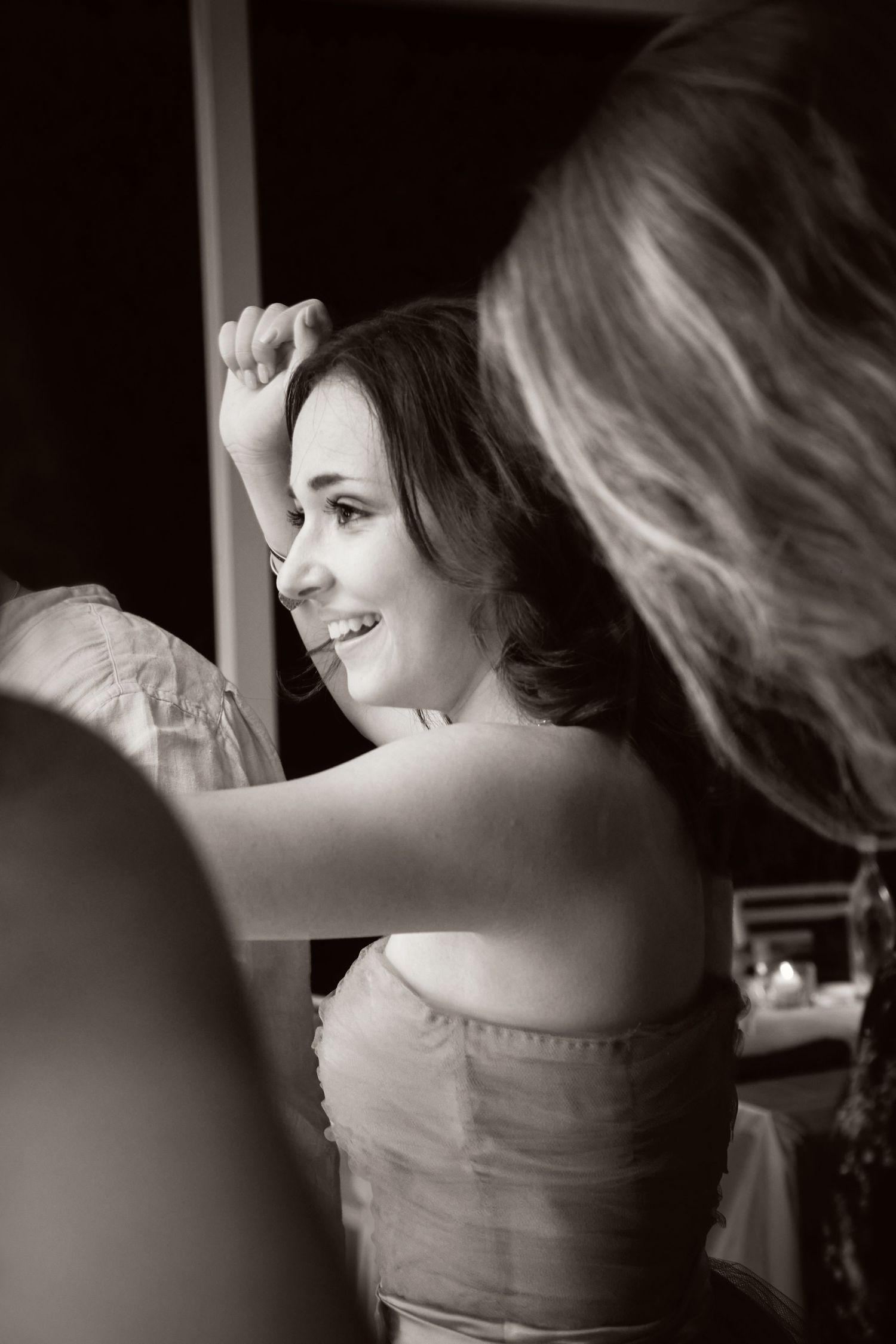 Black and white photo of a smiling brunette woman in a strapless dress at a celebration.