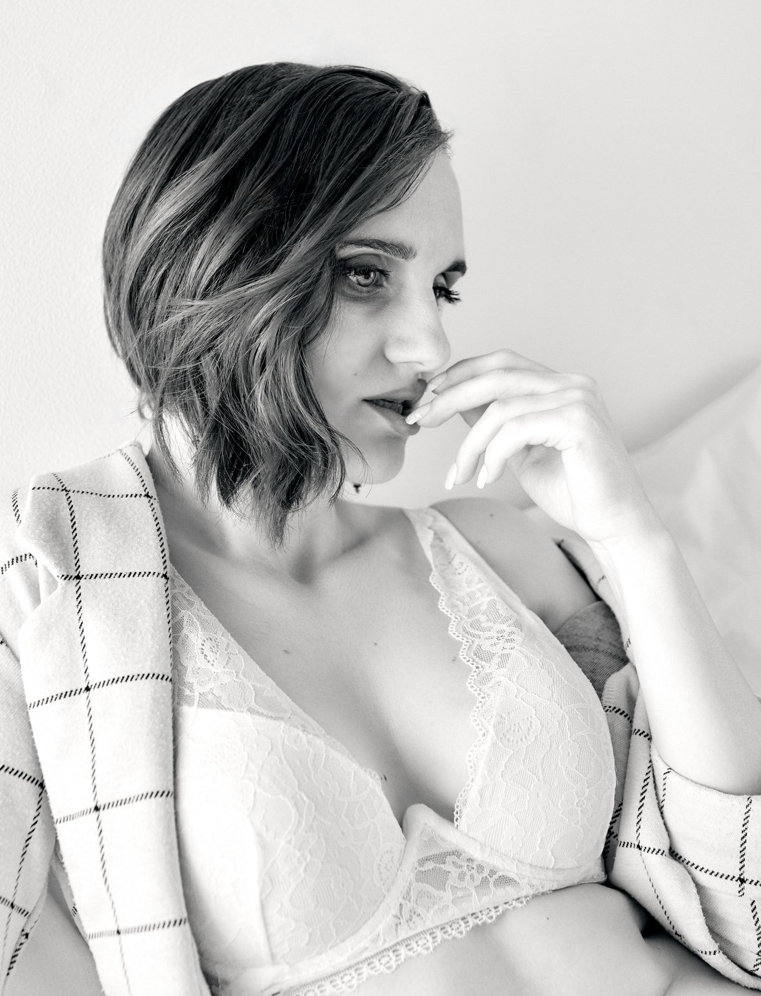 Black and white boudoir portrait of short-haired woman in lace bra resting chin on hand.
