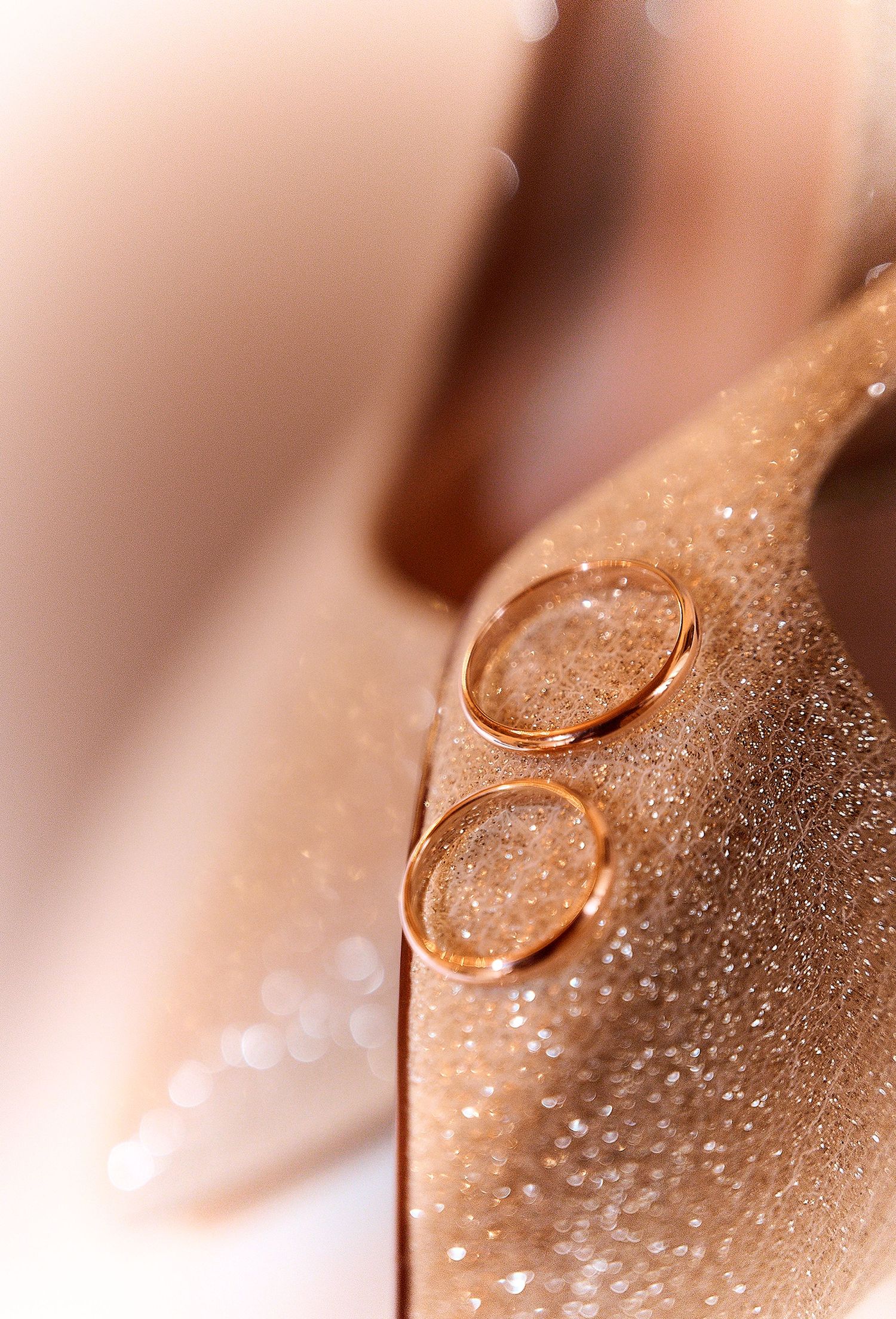Two gold wedding bands resting on a glittery rose gold high heel bridal shoe.