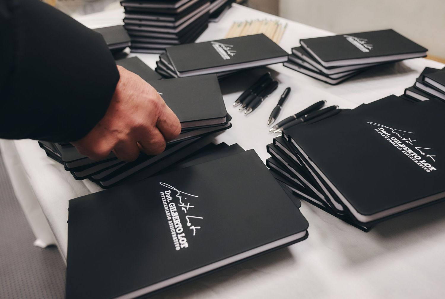 Stack of black branded notebooks and pens arranged on a white table at an event.