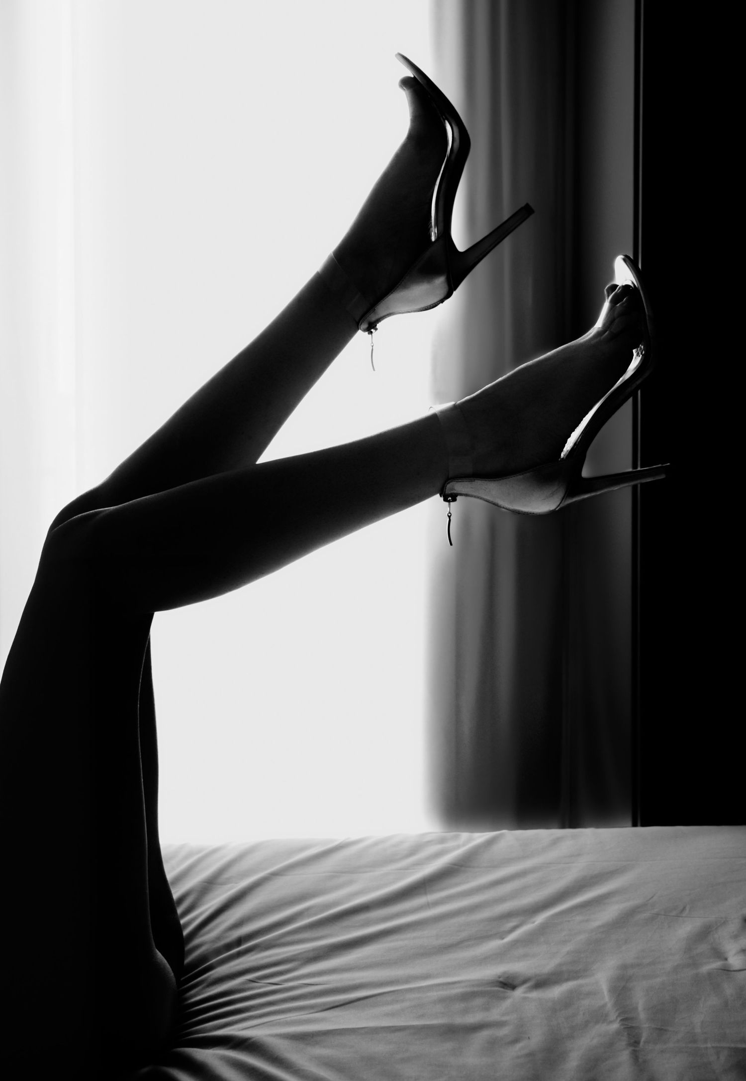 Black and white artistic photo of womans legs raised in high heels against bright window.