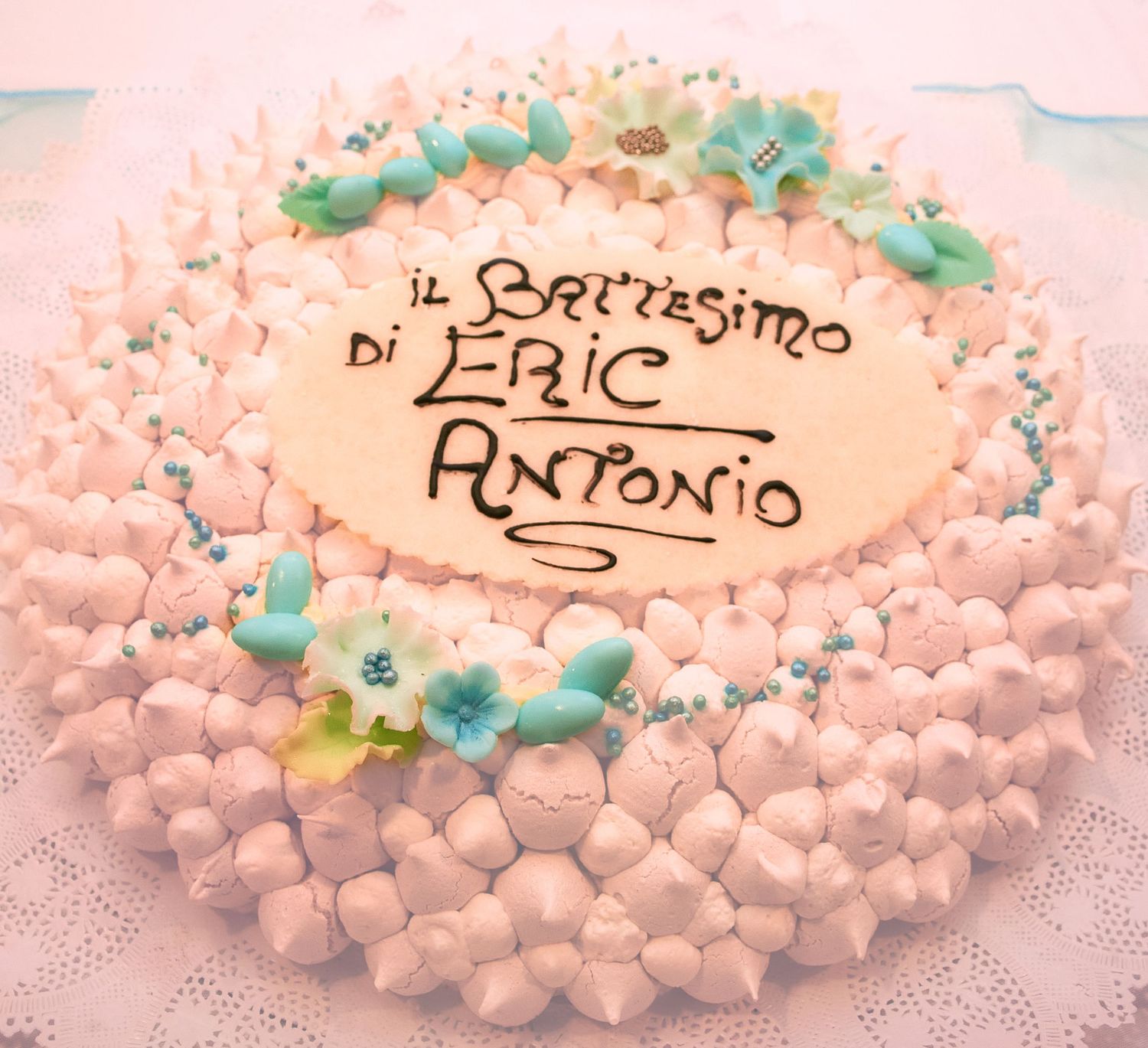 Pink baptism cake decorated with meringues and flowers reading Il Battesimo di Eric Antonio.
