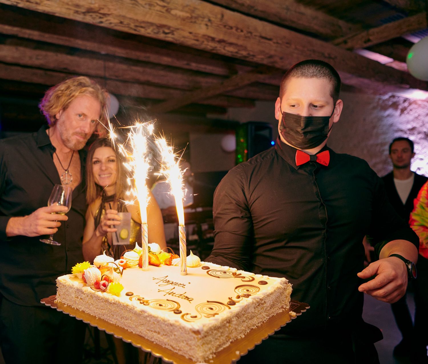 A masked server presents a birthday cake with sparklers at a celebratory party event.