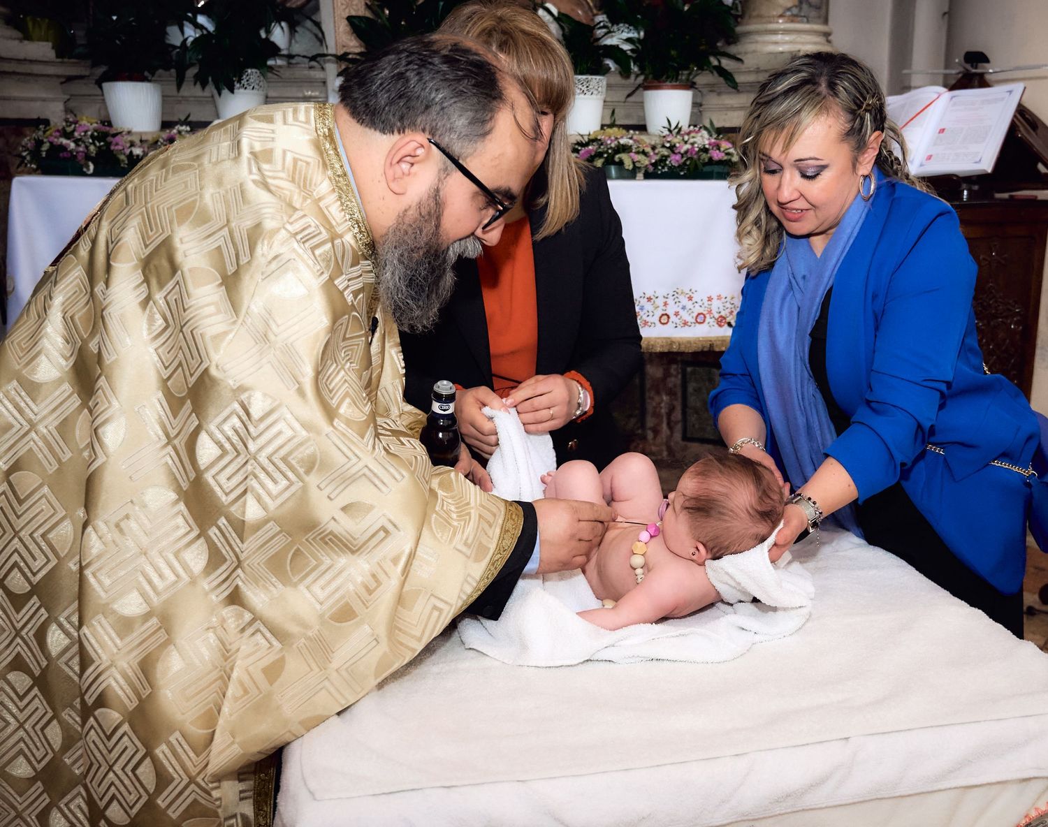 Orthodox priest performing baptism ceremony on infant baby at church altar.