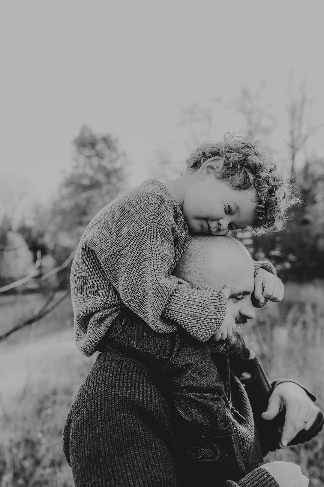 Black and white photo of a curly-haired child hugging an adult outdoors in a tender embrace.