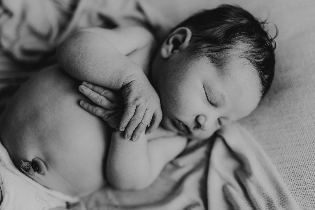 Black and white close-up of sleeping newborn baby curled up on soft blanket.