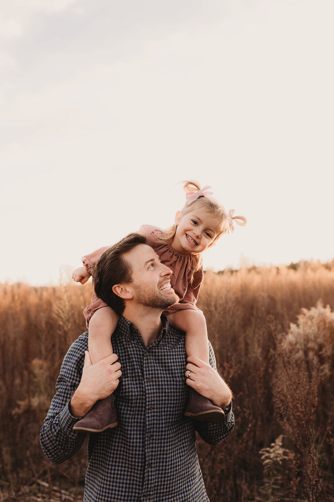 Smiling father carrying his little girl on his shoulders in an autumn field.