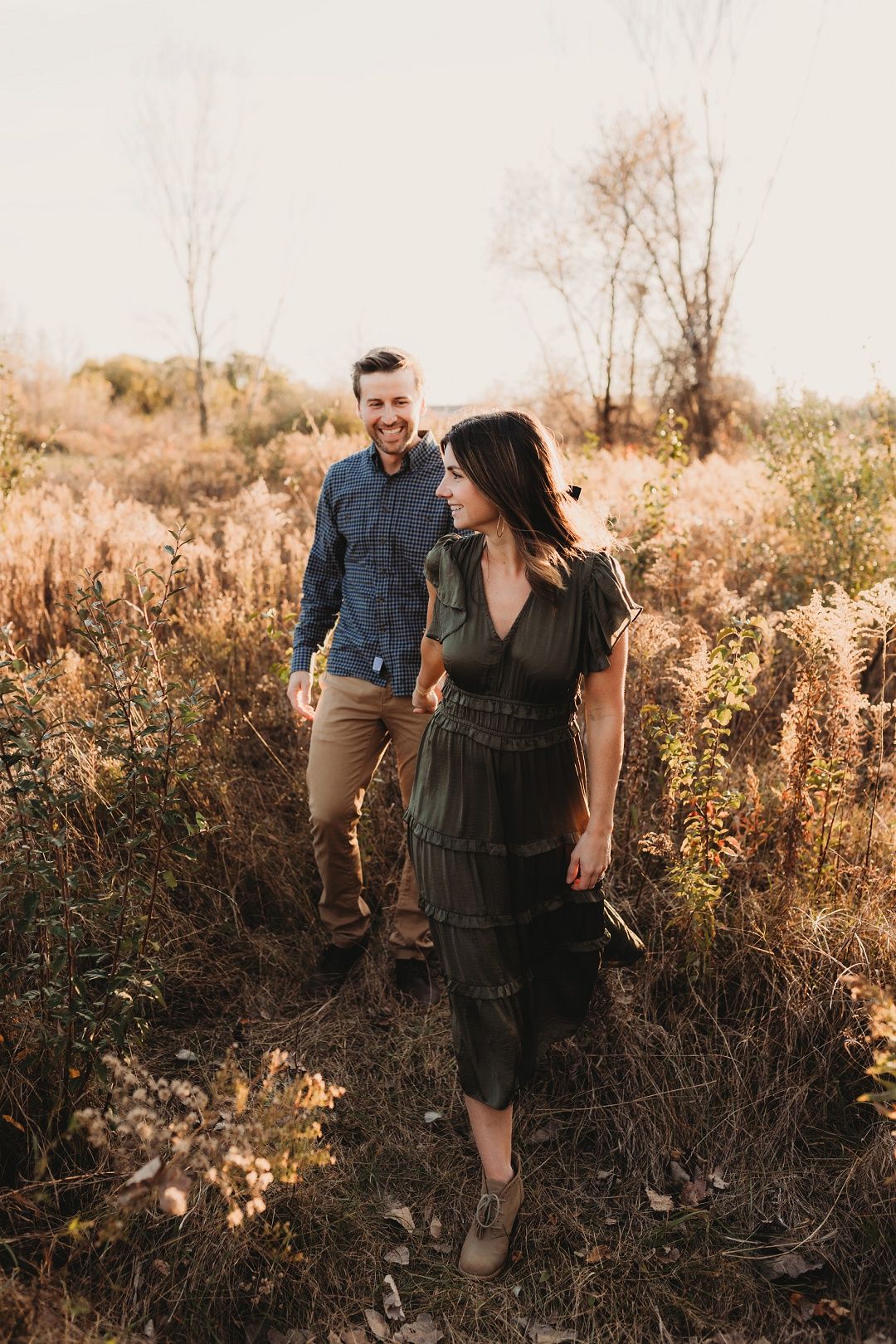 Couple walking through autumn wildflowers in a sun-drenched field at golden hour.