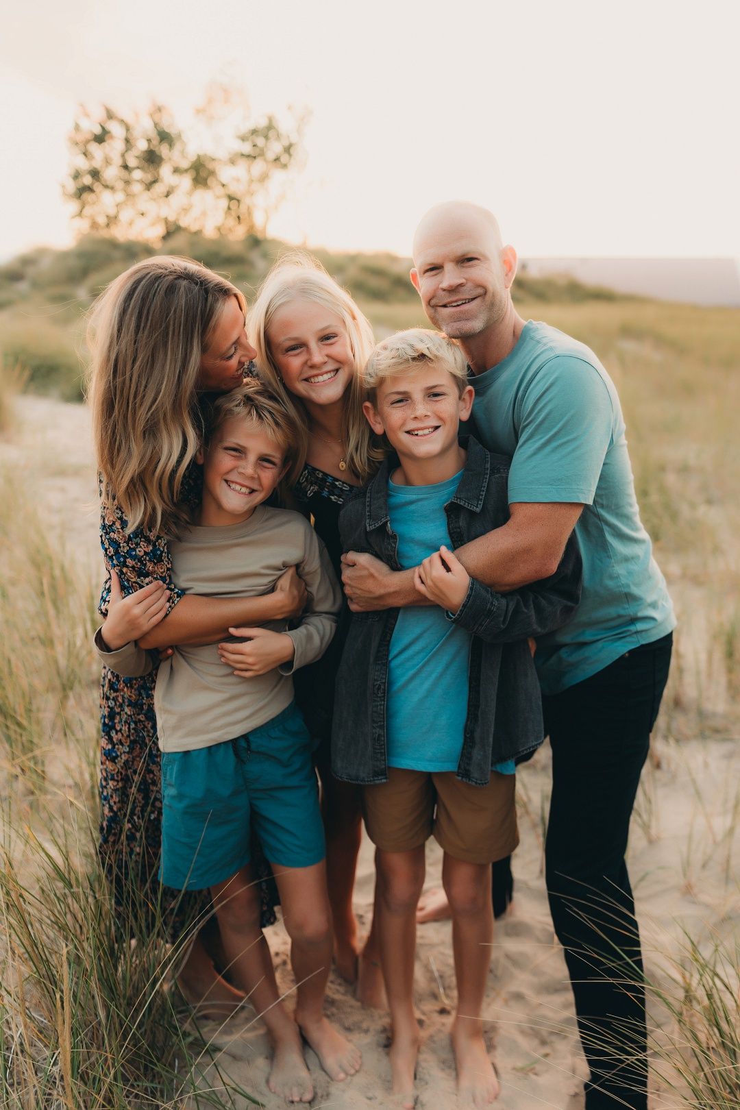 Happy family of five hugging together in sandy dunes at golden sunset.