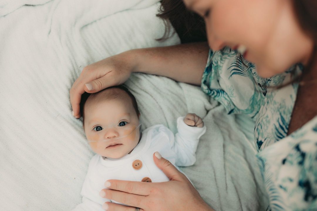 Mother tenderly touching her newborn baby's head as infant lies on white bedding looking up.