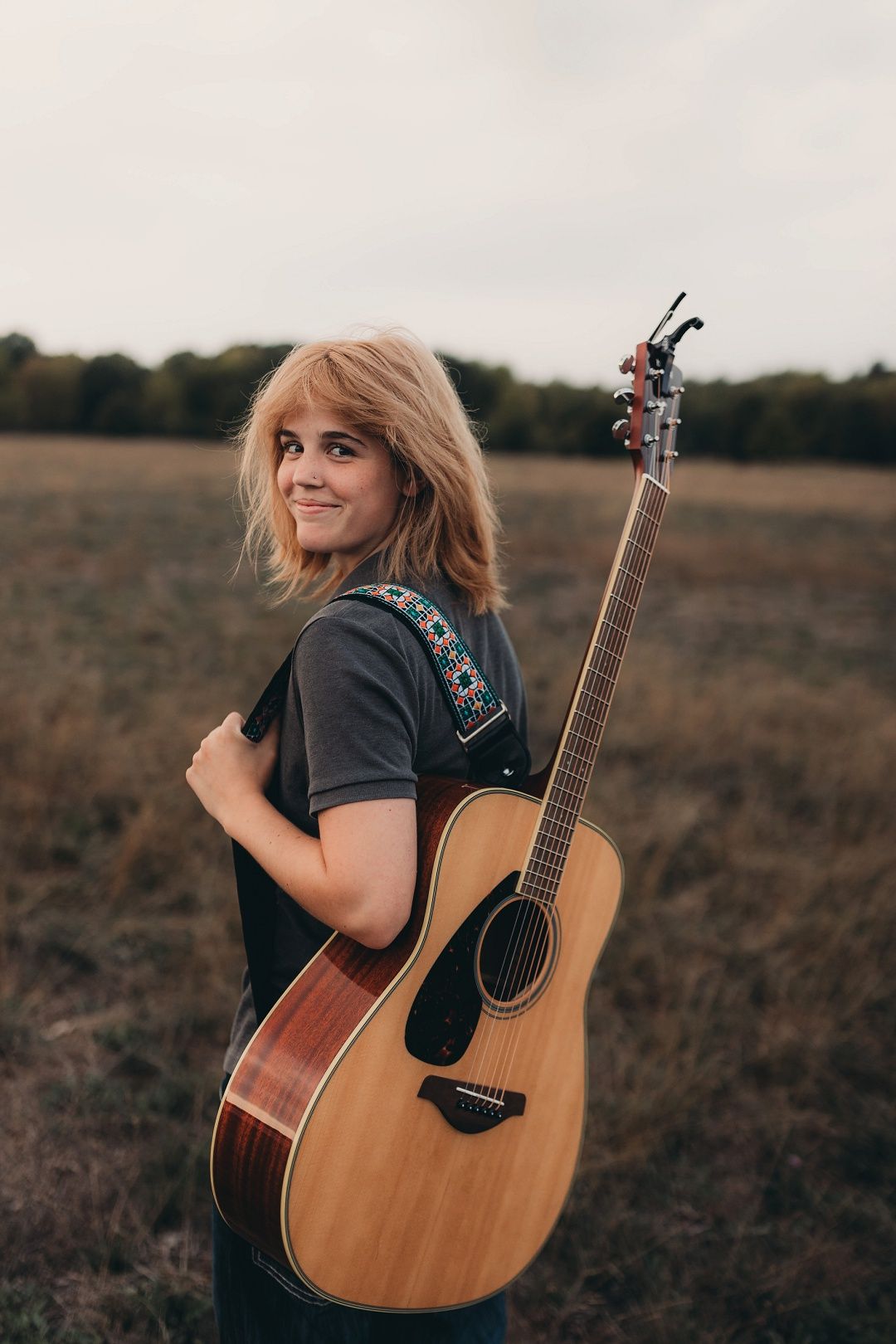 Blonde teen girl holding acoustic guitar in open field for senior portrait session.