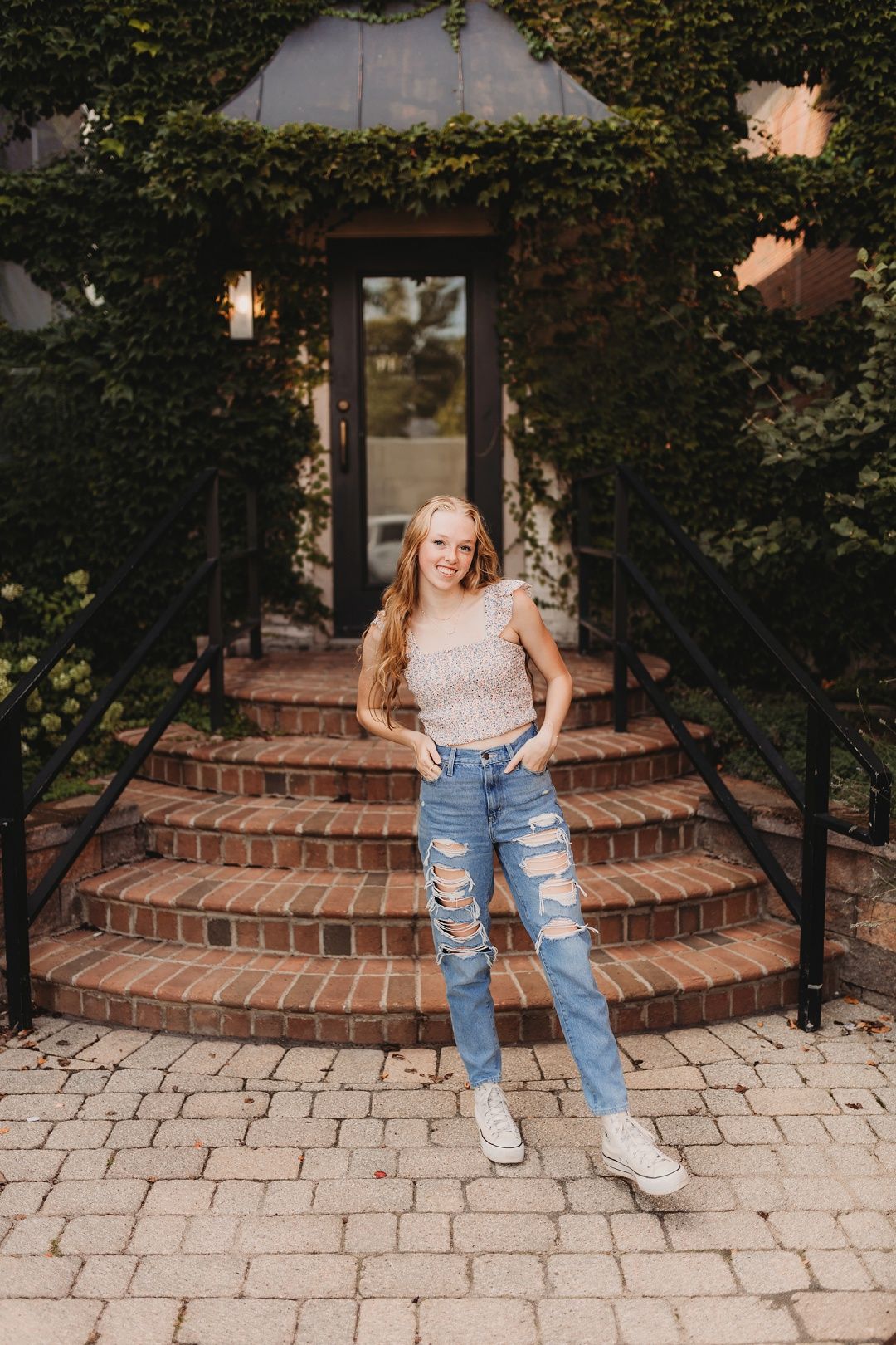 Teen girl in ripped jeans and crop top posing on brick steps.