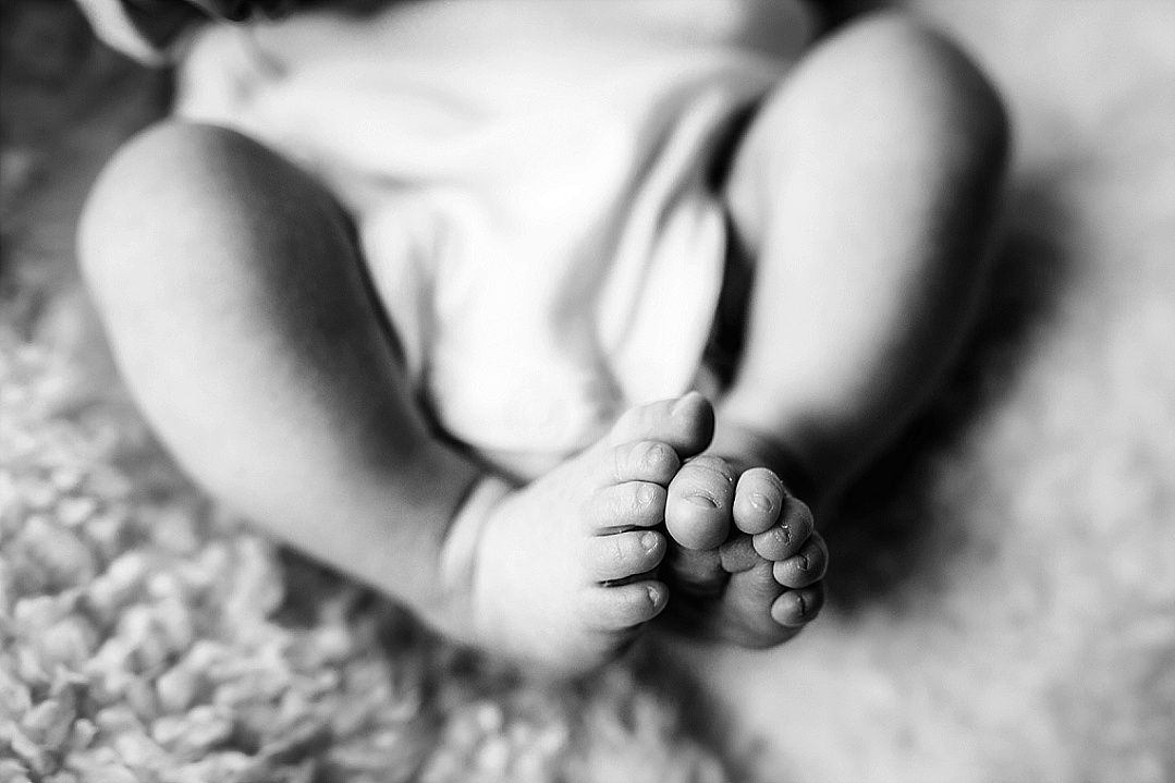 Black and white close-up photo of a newborn baby's tiny feet and toes on a soft rug.