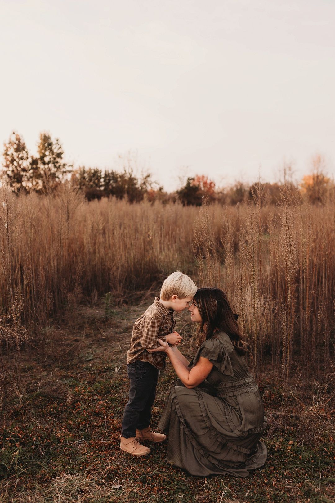 Mother crouching down to receive a kiss from her young son in a fall field.
