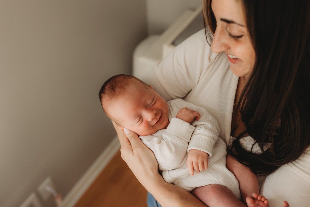 A dark-haired mother gently cradles her sleeping newborn baby in her arms.
