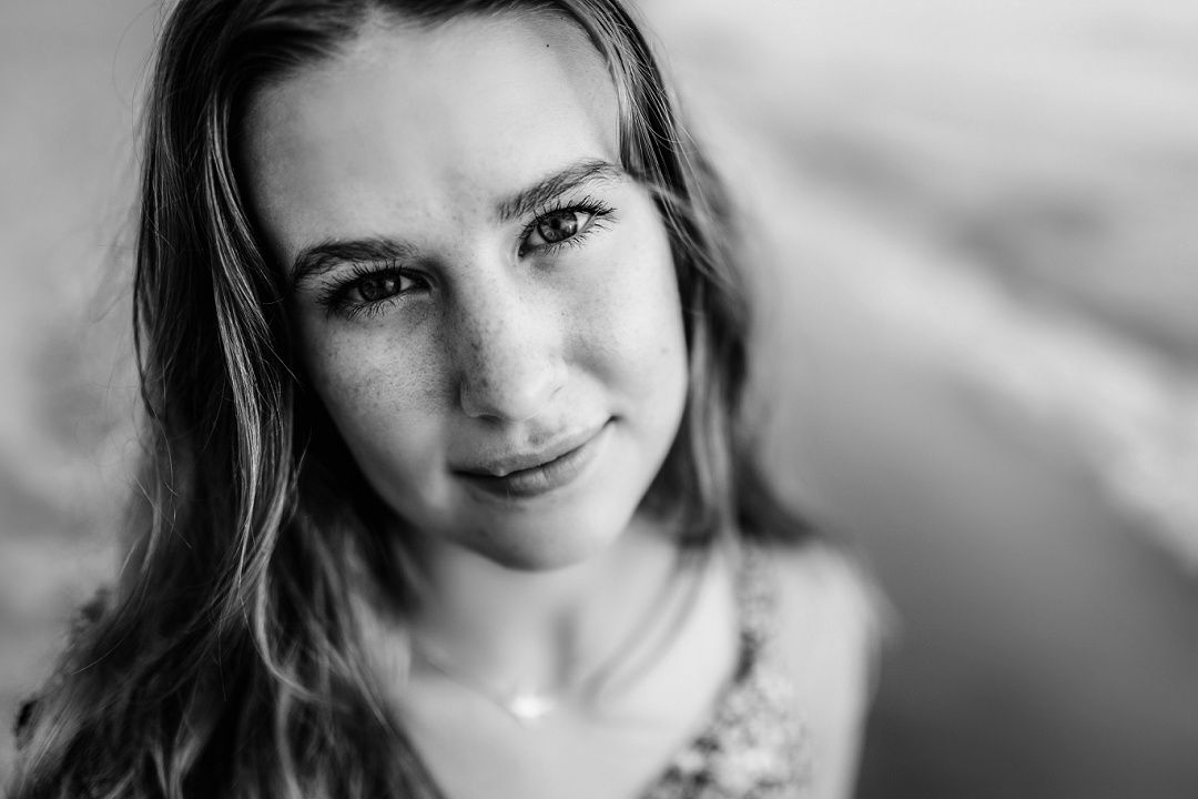Black and white close-up portrait of young woman with freckles and gentle smile, shallow depth of field.
