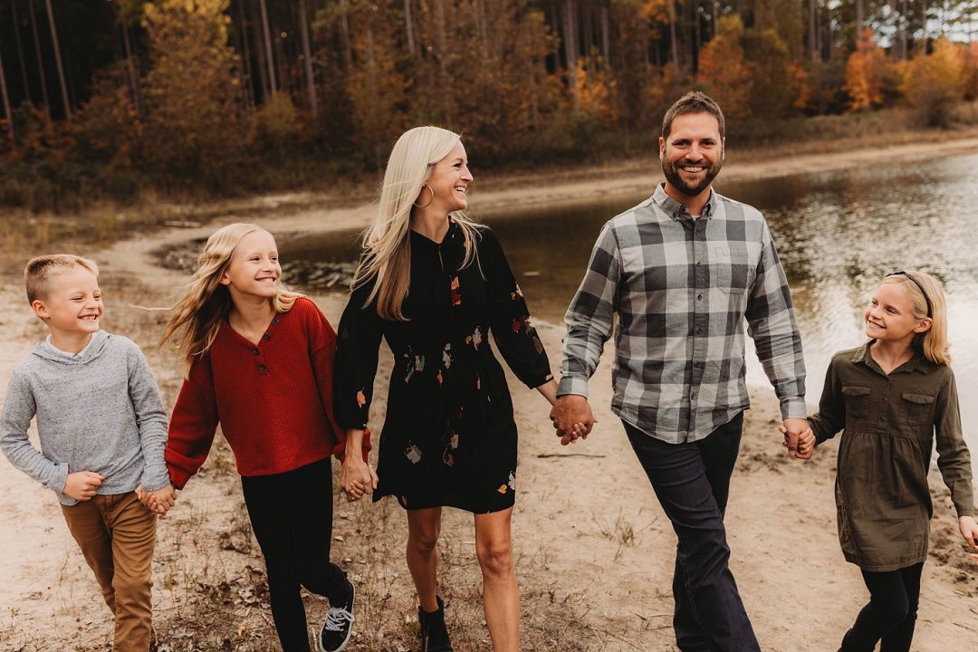 Family of five walking hand in hand along a scenic autumn forest path together.