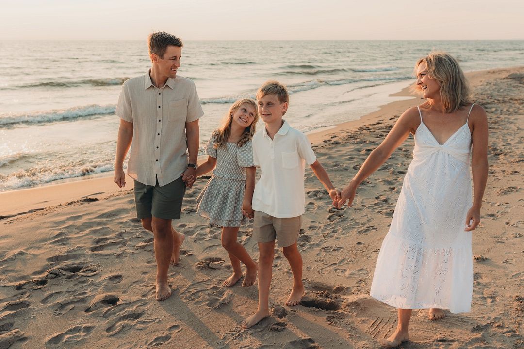 A happy family of four walks hand in hand along a sandy beach at sunset.