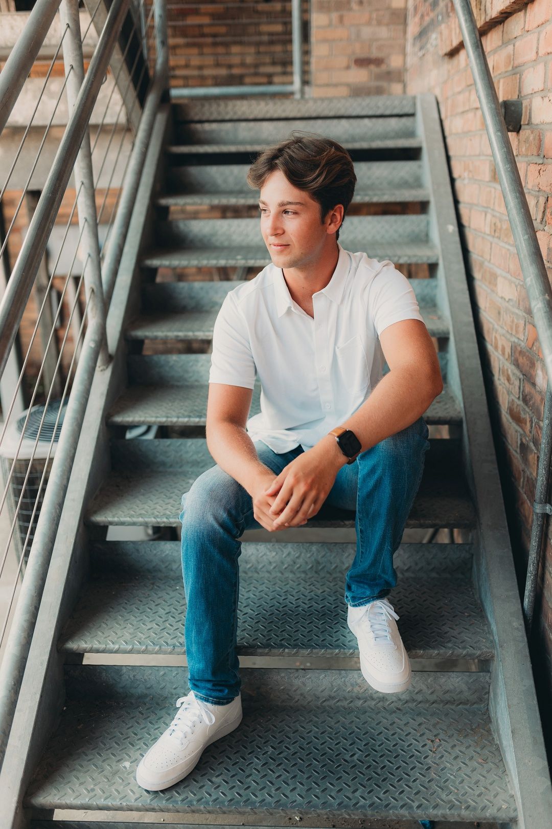 Young man in white shirt and jeans sitting on metal staircase.