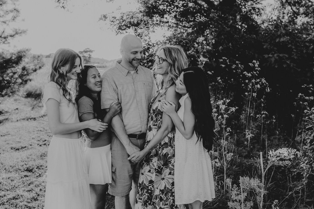 Black and white photo of a family of four sharing a warm embrace outdoors.