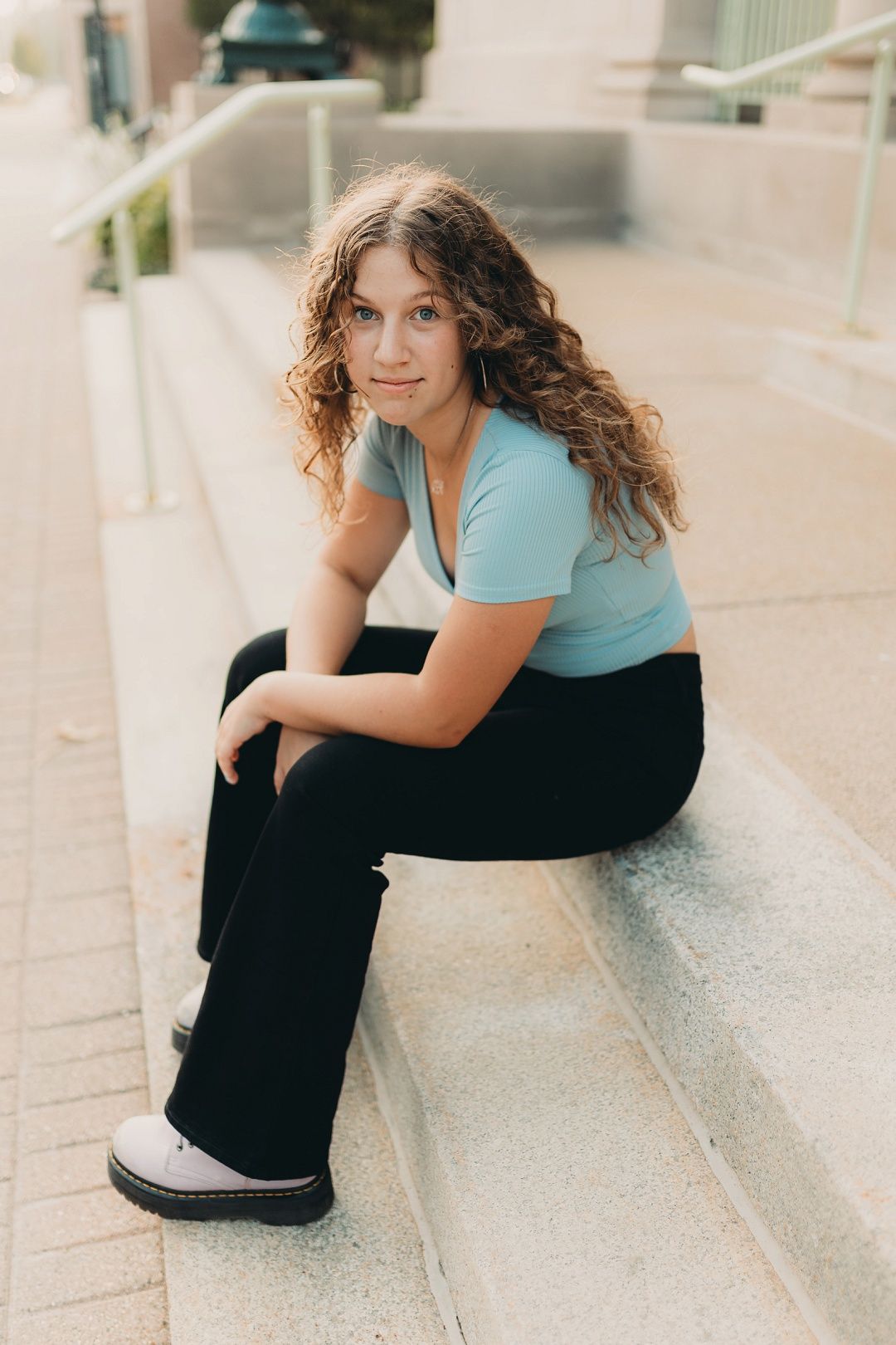 Teen girl with curly hair in blue top sitting on outdoor steps.