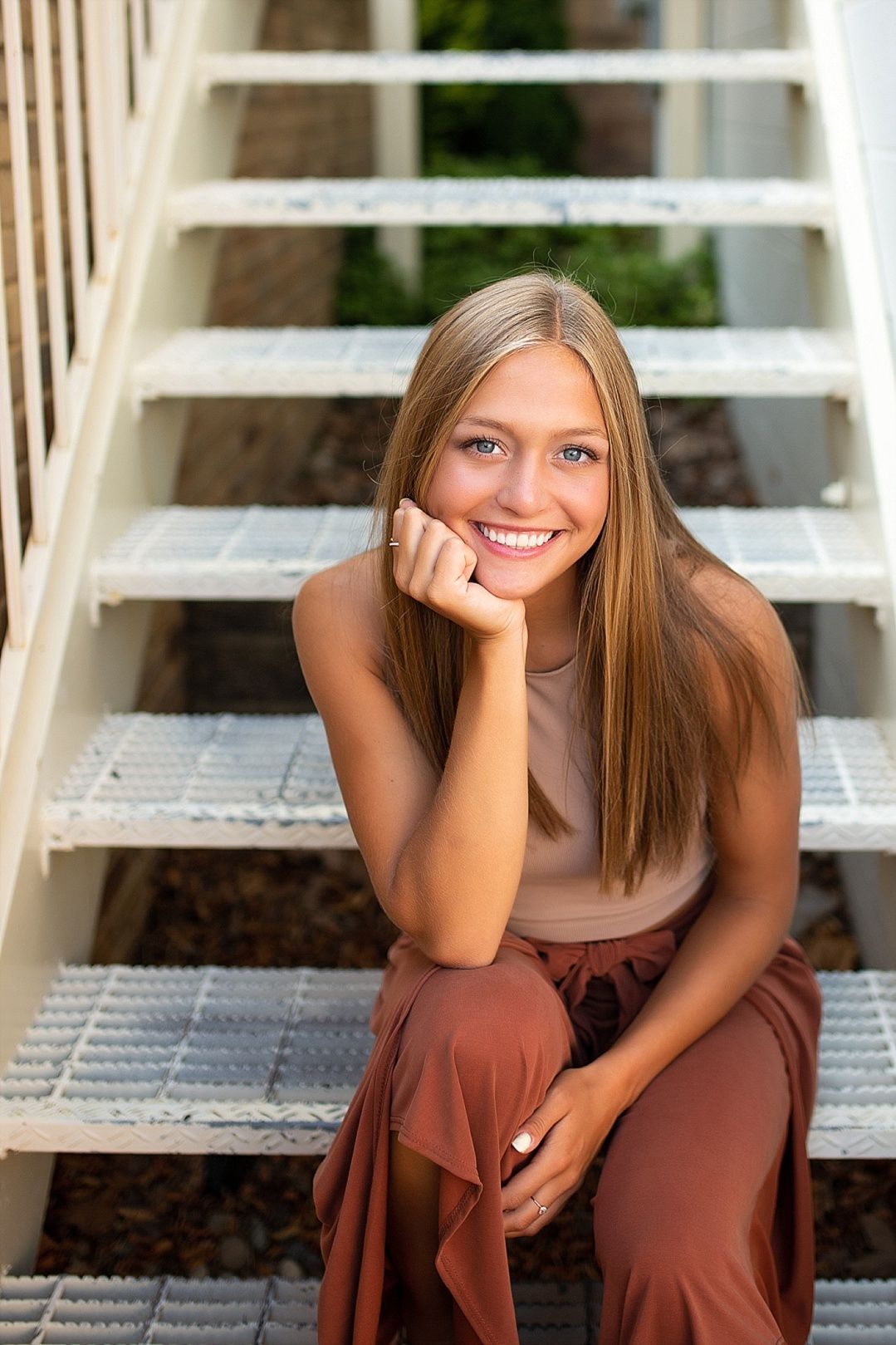 Blonde teenage girl with blue eyes smiling while sitting on white outdoor stairs.