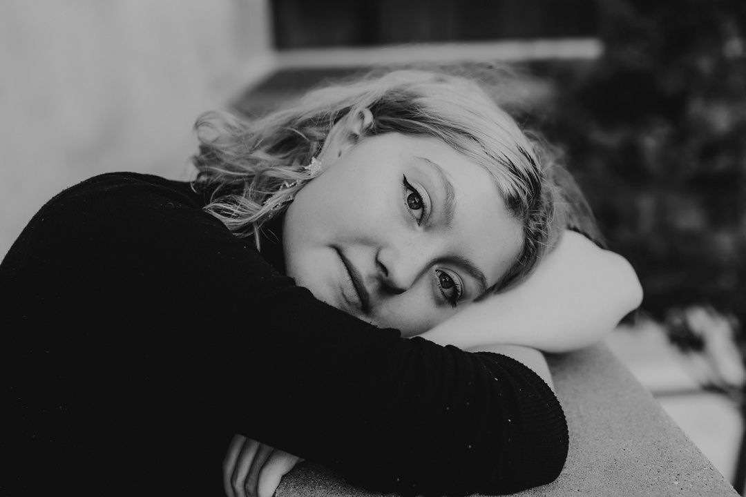 Black and white portrait of blonde woman resting head on arms, soft contemplative expression.