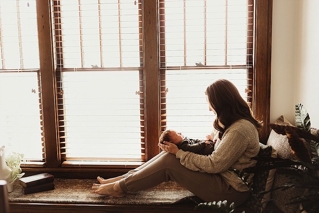 A young woman sits peacefully on a window bench holding a warm mug in soft natural light.