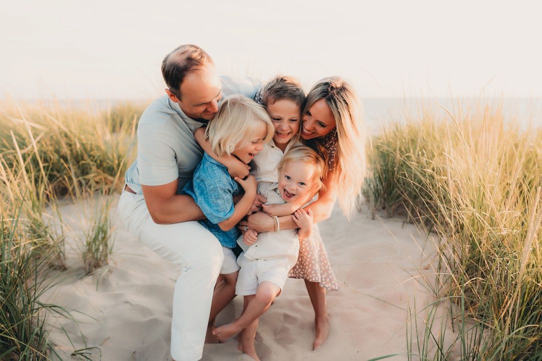 Happy family of five sharing a joyful group hug on a sandy beach at sunset.