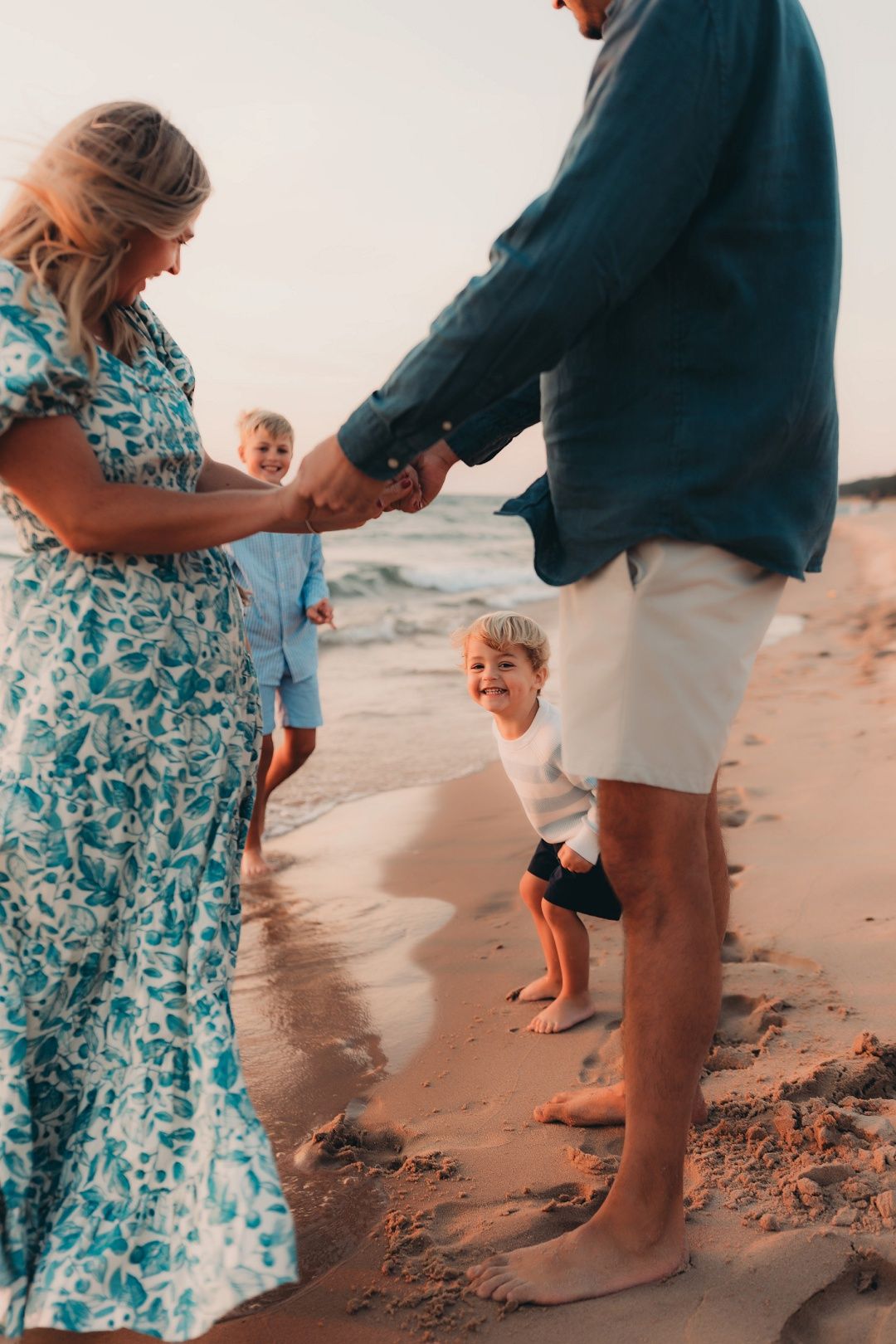 Family of four playing on sandy beach at sunset, child swinging between parents.