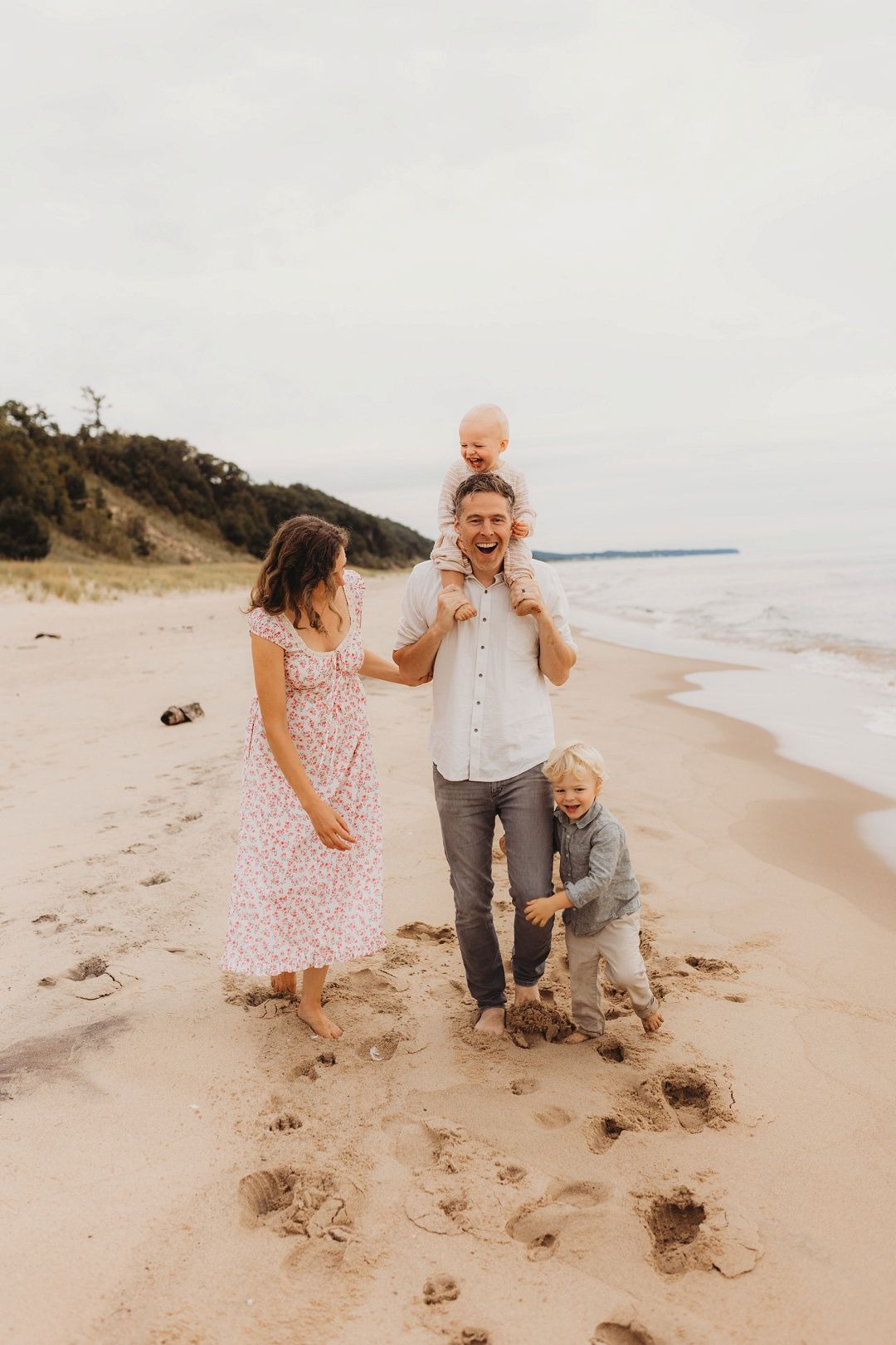 Happy family of four laughing and playing together on a sandy beach shoreline.