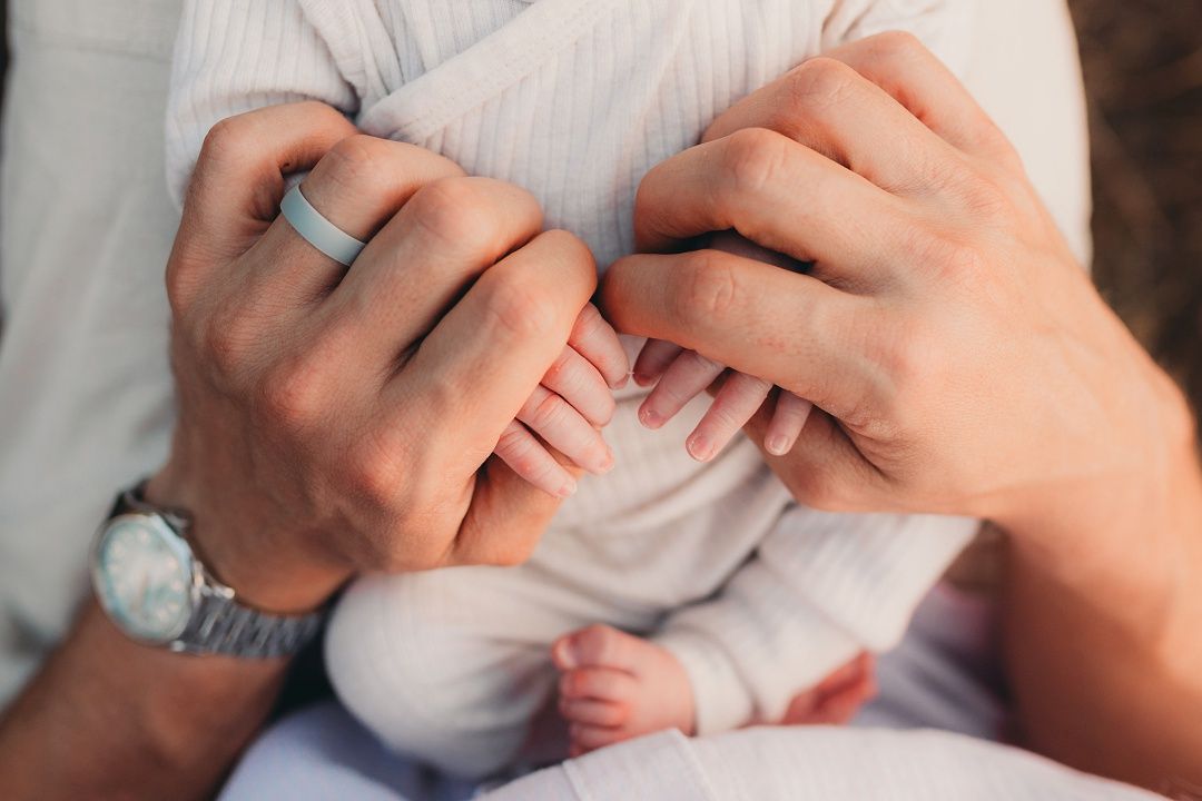 Two parents tenderly hold their newborn babys tiny hand together outdoors.
