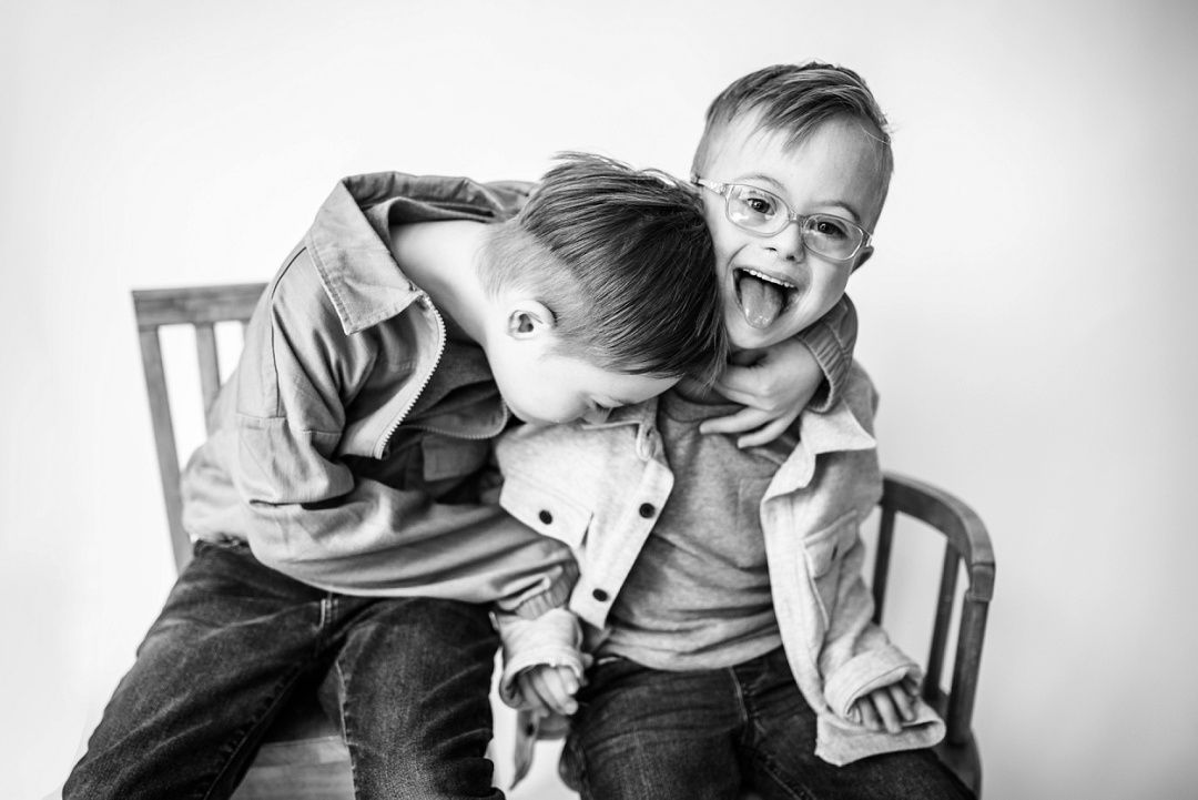 Two young brothers laughing and hugging playfully in a black and white portrait.