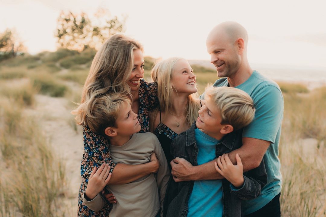 A family of five shares a warm group hug among golden grass dunes at sunset.