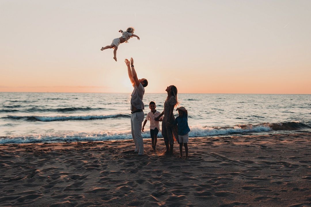 Family on beach at sunset with parent tossing child in the air joyfully.