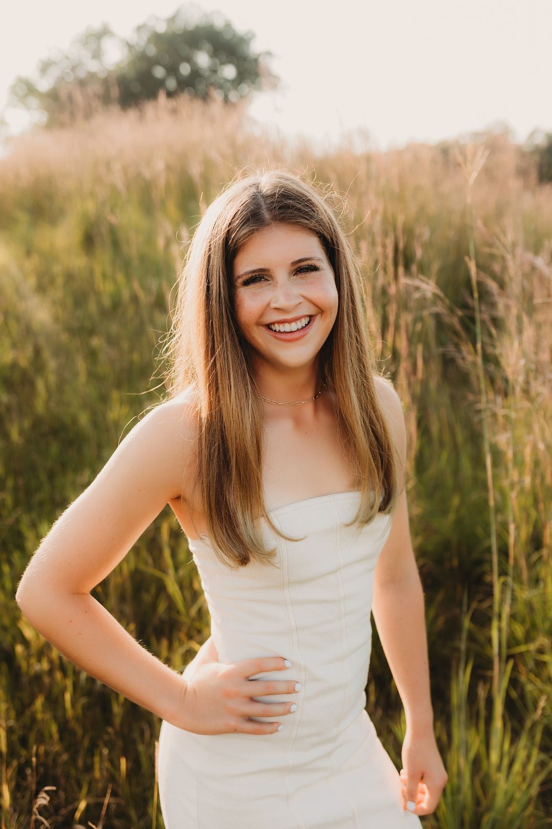 Young woman in white strapless dress smiling in golden hour field.