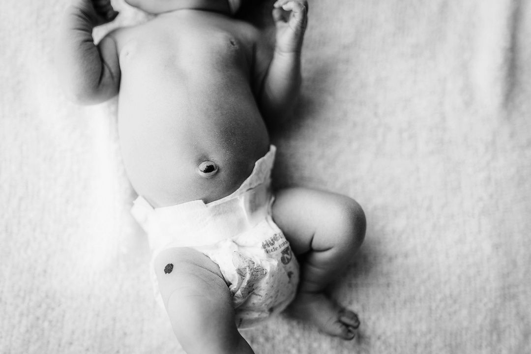 Black and white close-up of newborn baby lying on soft blanket wearing diaper, showing belly button.