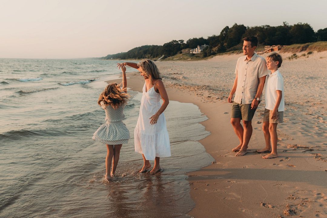Family of four enjoys playful moment together on sandy beach at sunset.
